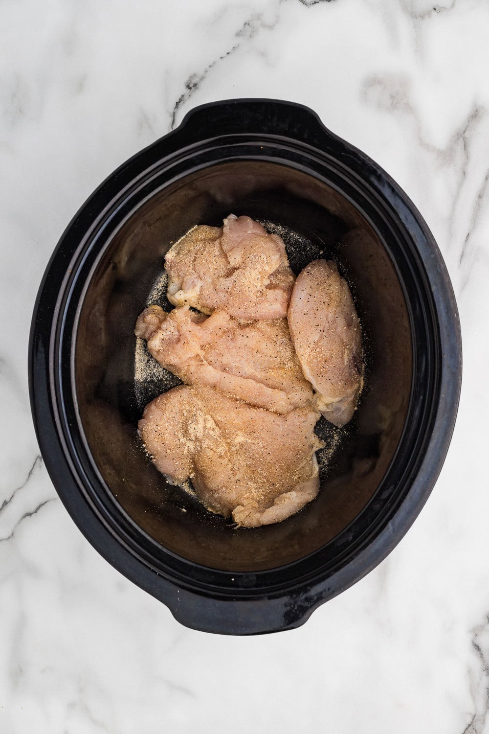 A slow cooker filled with raw chicken