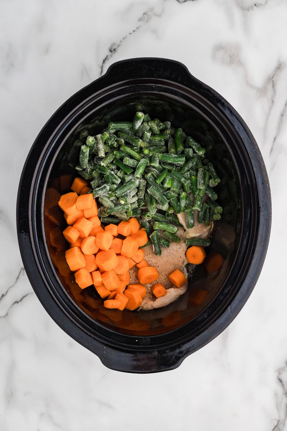 A slow cooker filled with carrots, green beans and other vegetables