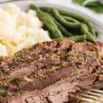 Sliced flank steak and mashed potatoes on a plate with green beans and a slow cooker