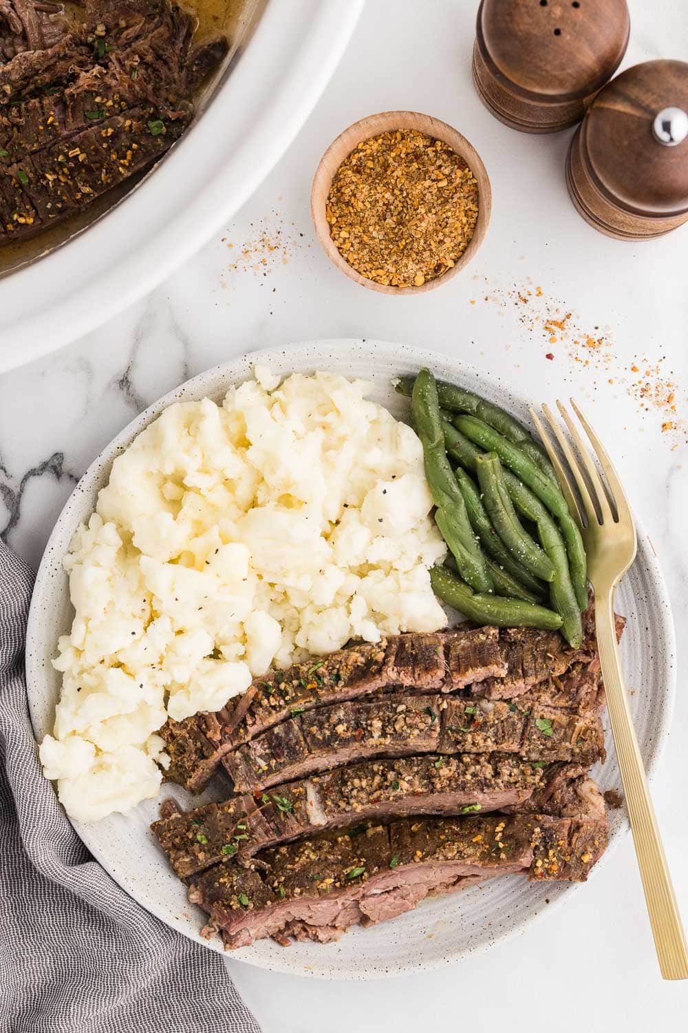 Sliced flank steak and mashed potatoes on a plate with green beans and a slow cooker