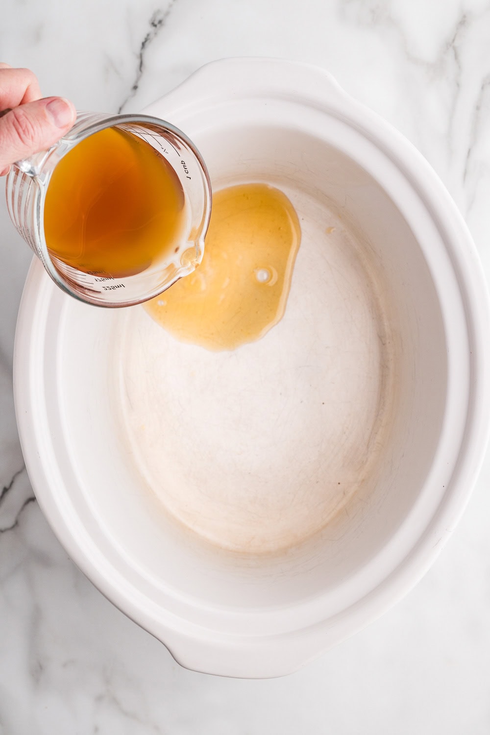 A hand pouring broth into a slow cooker