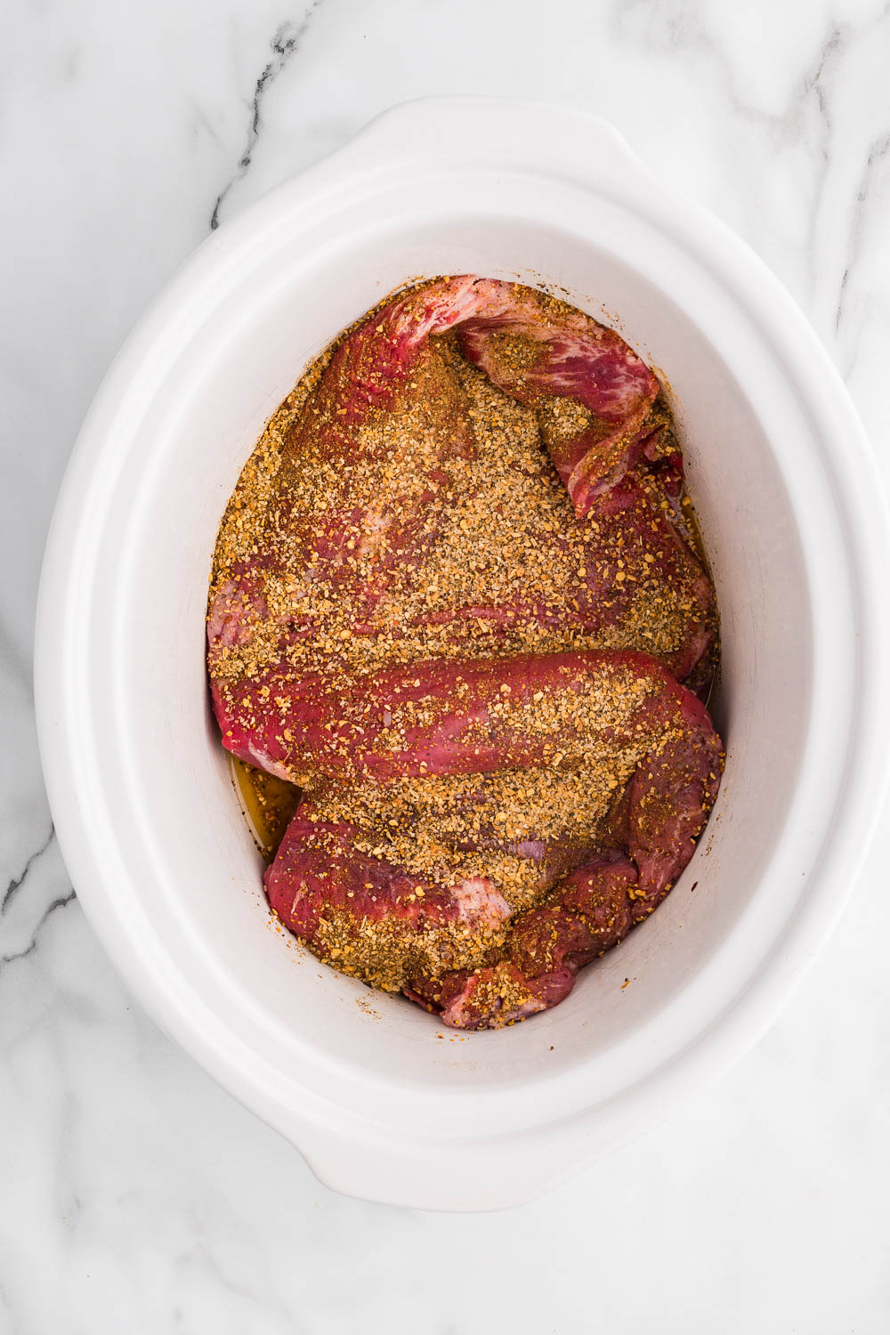 A large piece of flank steak in a white slow cooker