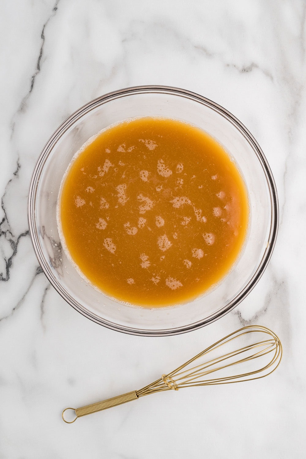 Chicken broth inside of bowl next to whisk