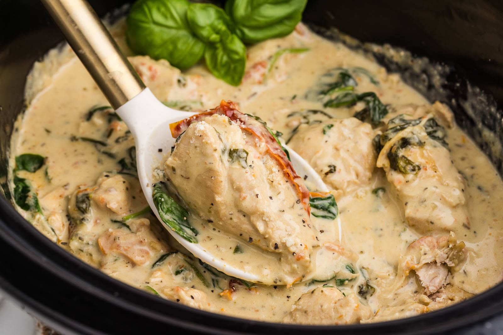 closeup shot of Tuscan chicken in black slow cooker and white ladle