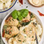 overhead plated Tuscan chicken on bed of mashed potatoes in white bowl, with bowls of mashed potatoes and Parmesan cheese in background