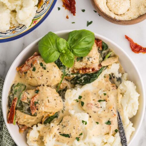 overhead plated Tuscan chicken on bed of mashed potatoes in white bowl, with bowls of mashed potatoes and Parmesan cheese in background
