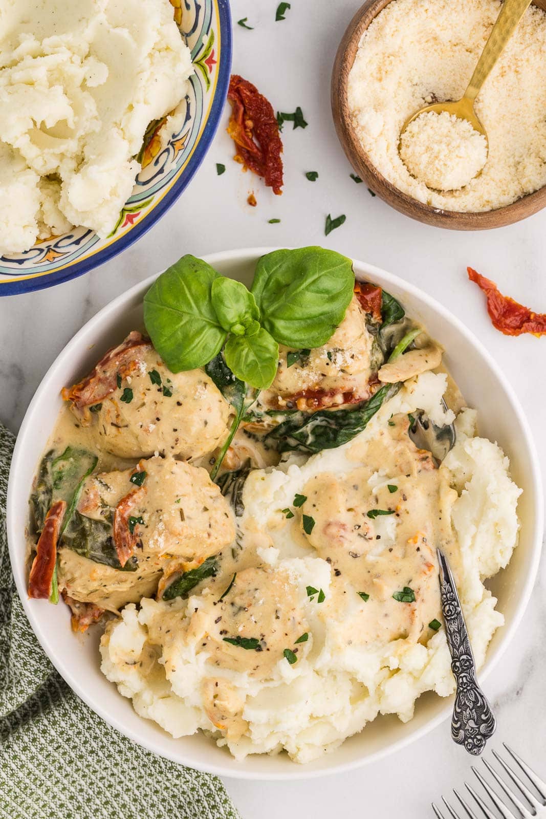 overhead plated Tuscan chicken on bed of mashed potatoes in white bowl, with bowls of mashed potatoes and Parmesan cheese in background