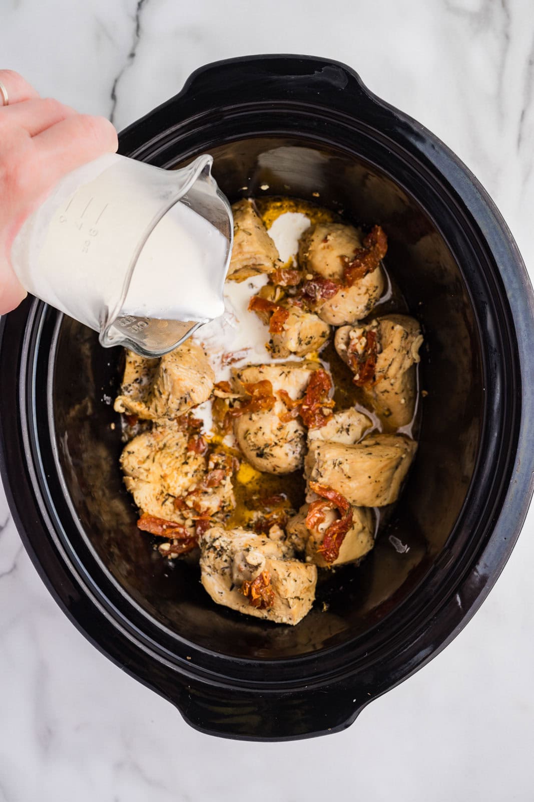 black slow cooker with cooked chicken and addition of heavy cream