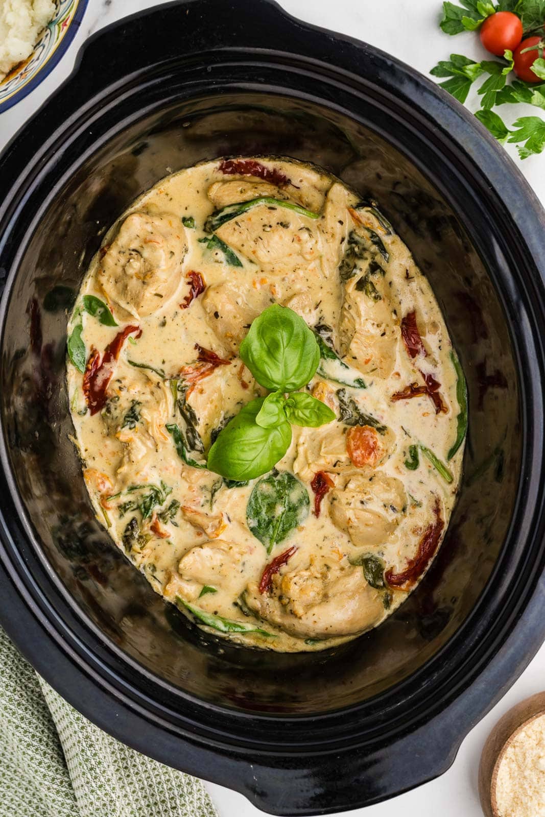overhead shot of black slow cooker with finished Tuscan chicken and basil leaves