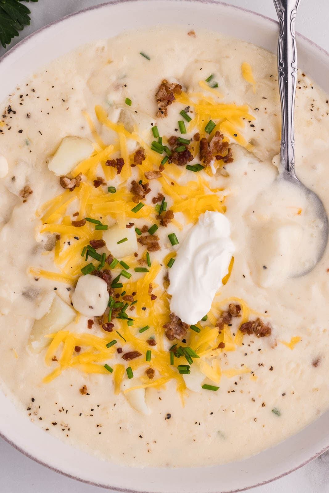 overhead shot of white bowl with silver spoon containing garnished potato soup