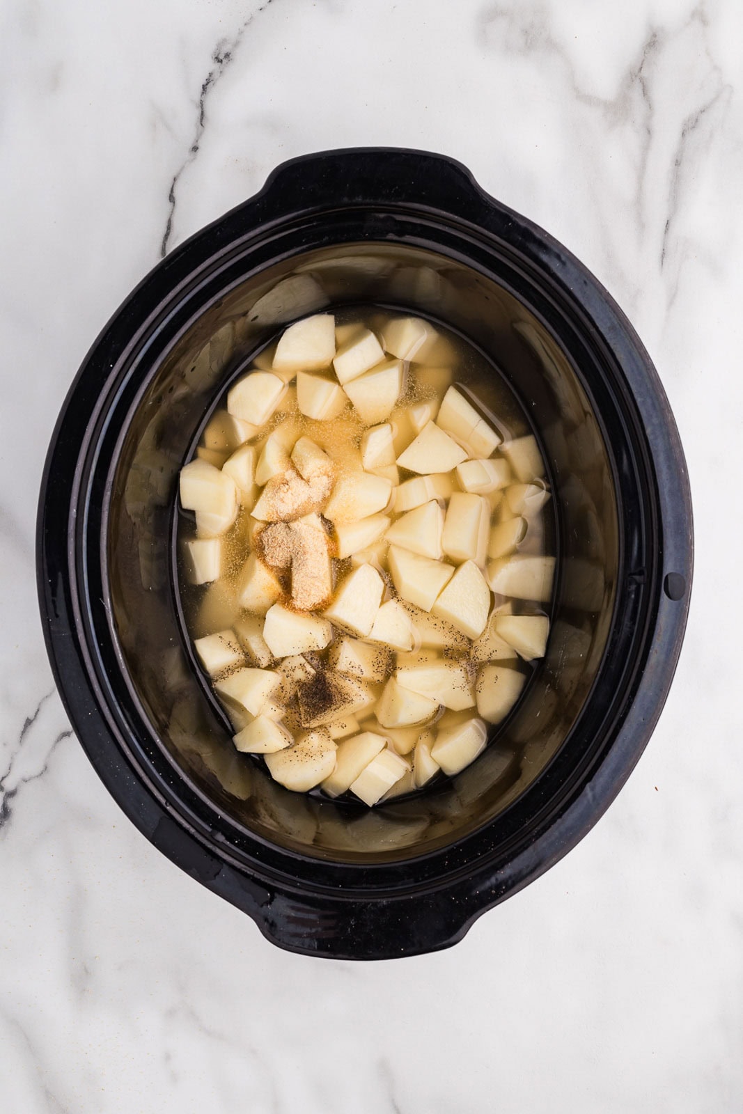 black slow cooker with cut up potatoes in broth and seasonings