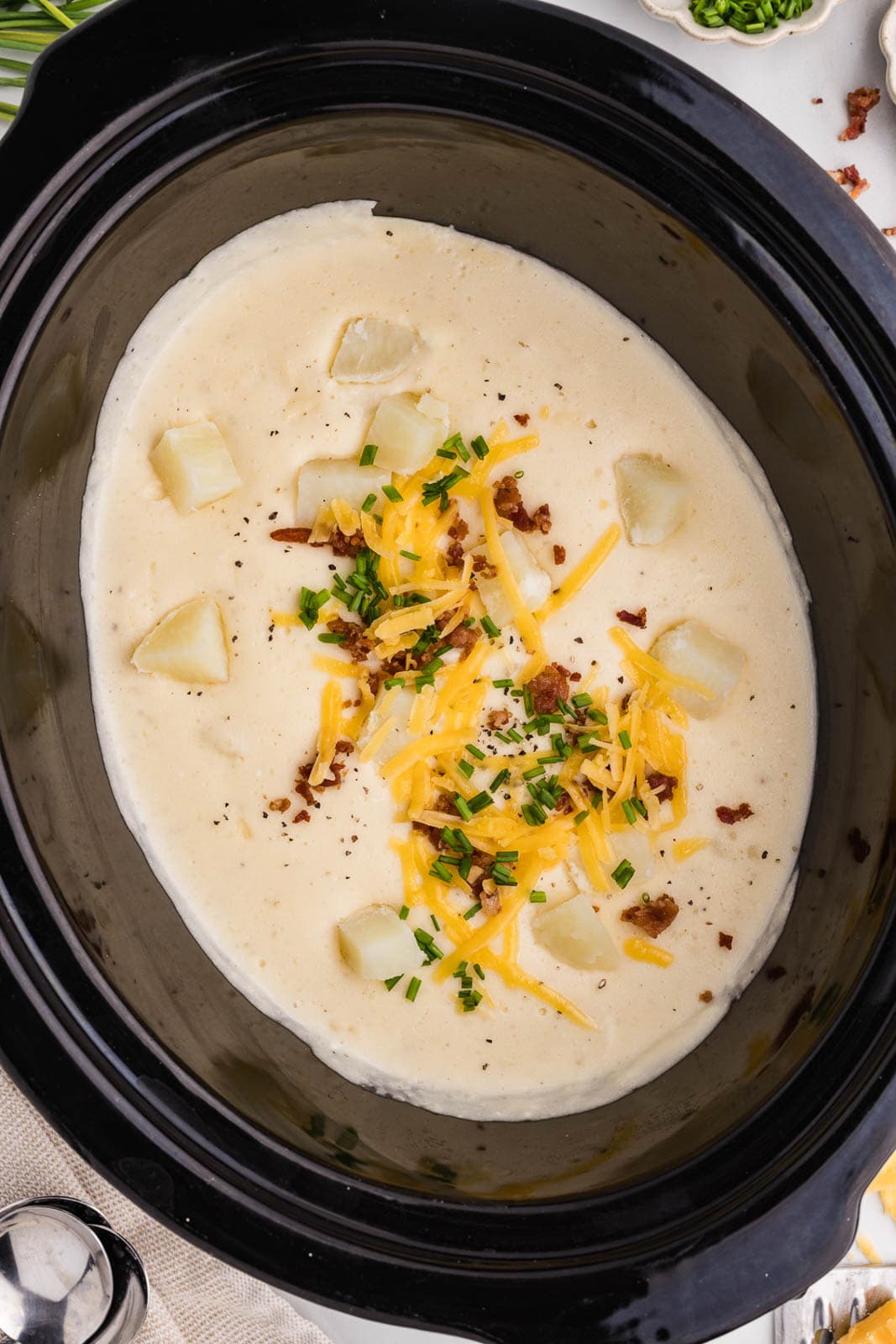 overhead shot of slow cooker containing potato soup, garnished with green onion, crumbled bacon and extra cheese