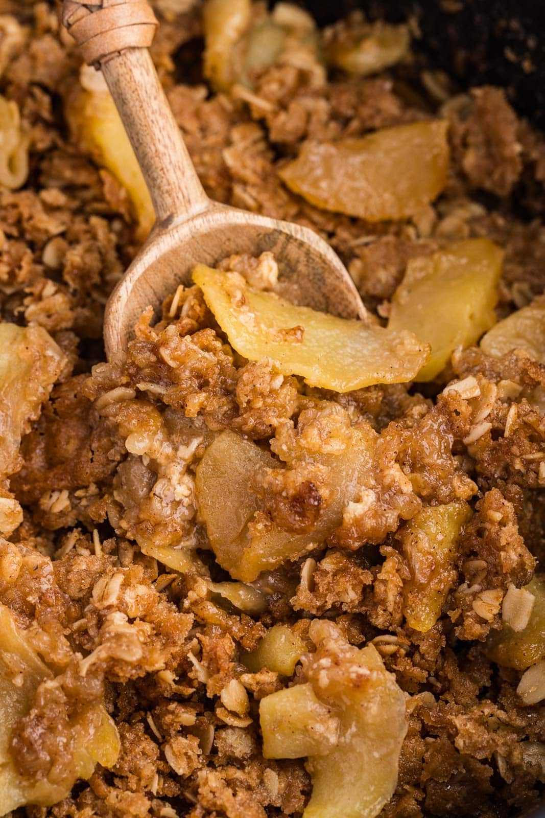 Apple crisp in a slow cooker being scooped on wooden spoon