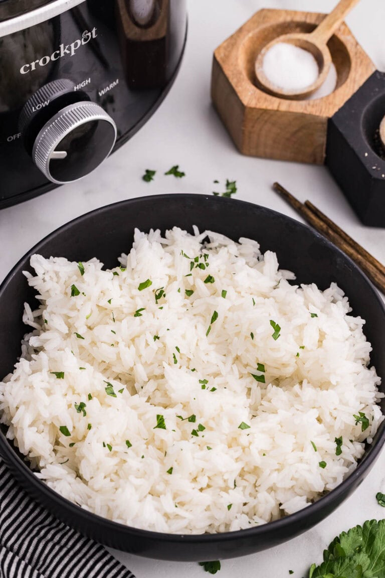 black bowl of cooked rice with cilantro, surrounded by crockpot, salt and pepper containers with spoons, chopsticks, sprig of cilantro and black and white dish towel