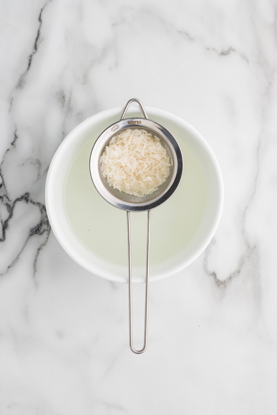 rice filled strainer over a white bowl of water