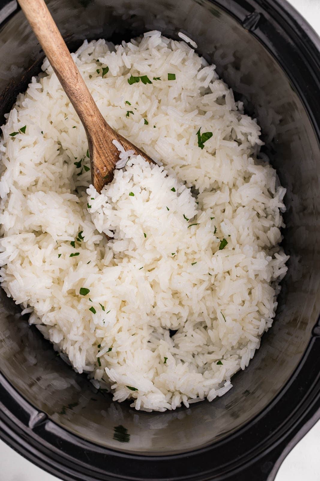 closeup view of cooked white rice with cilantro, wooden spoon in black slow cooker