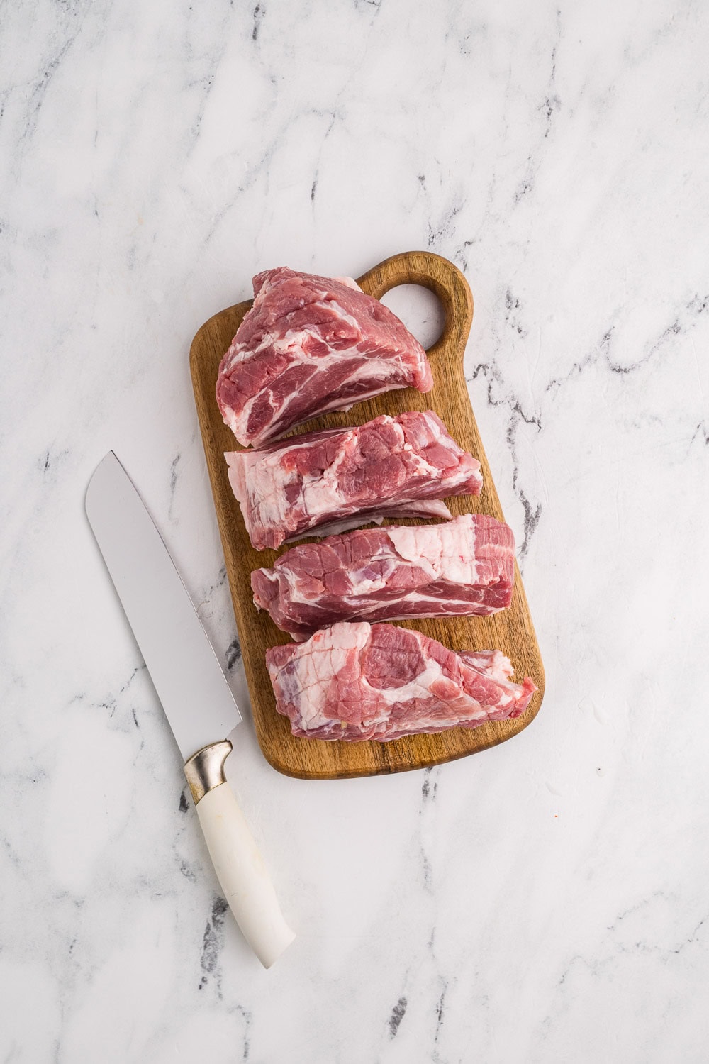 wooden cutting board with cut up pork with knife on left side