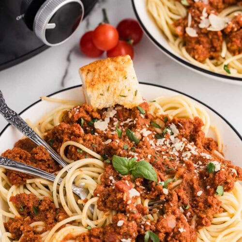 spaghetti sauce with pasta and two forks on white plate with slow cooker in background