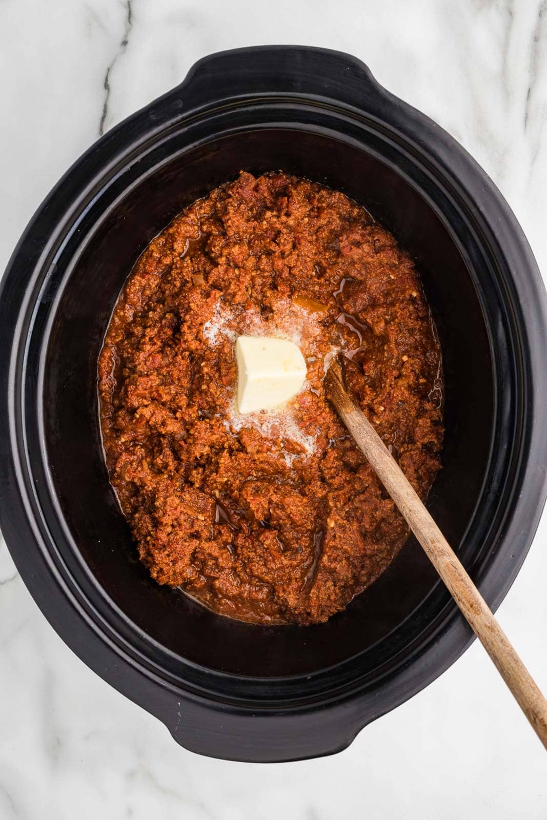 slow cooker with finished spaghetti sauce with wooden spoon and butter