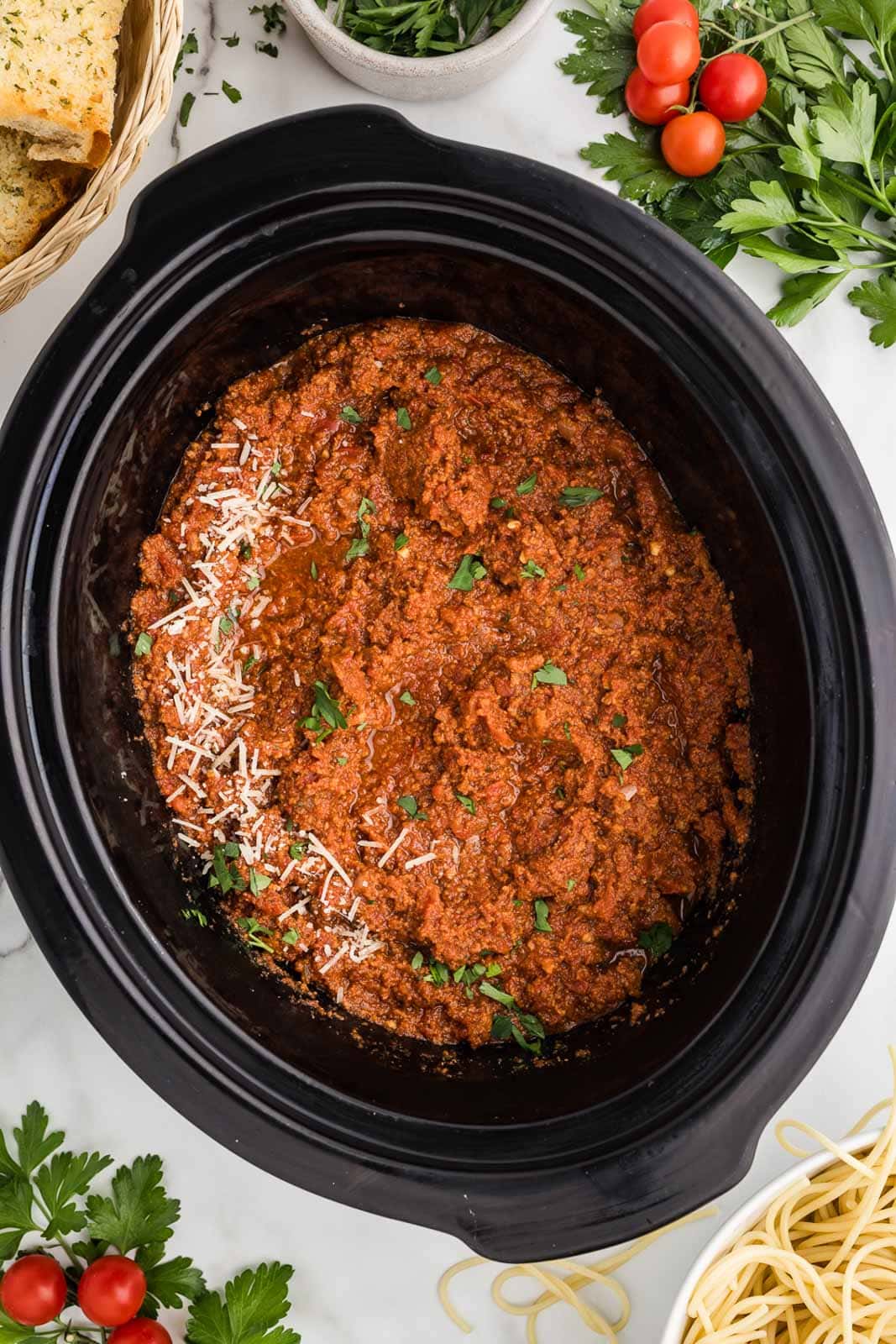 overhead shot of slow cooker with completed spaghetti sauce with bread, basil and tomatoes in background