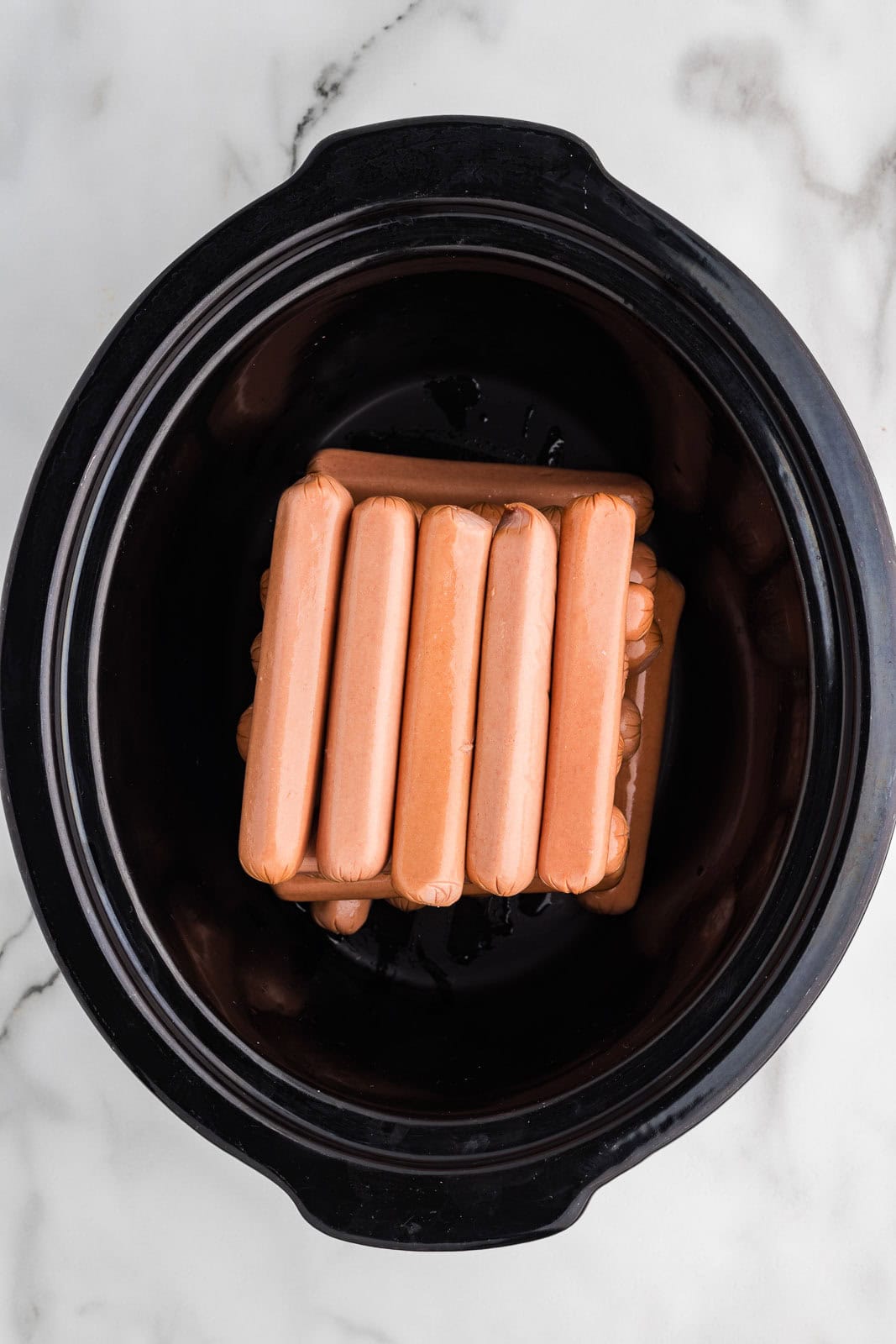black slow cooker with 24 hots dogs layered