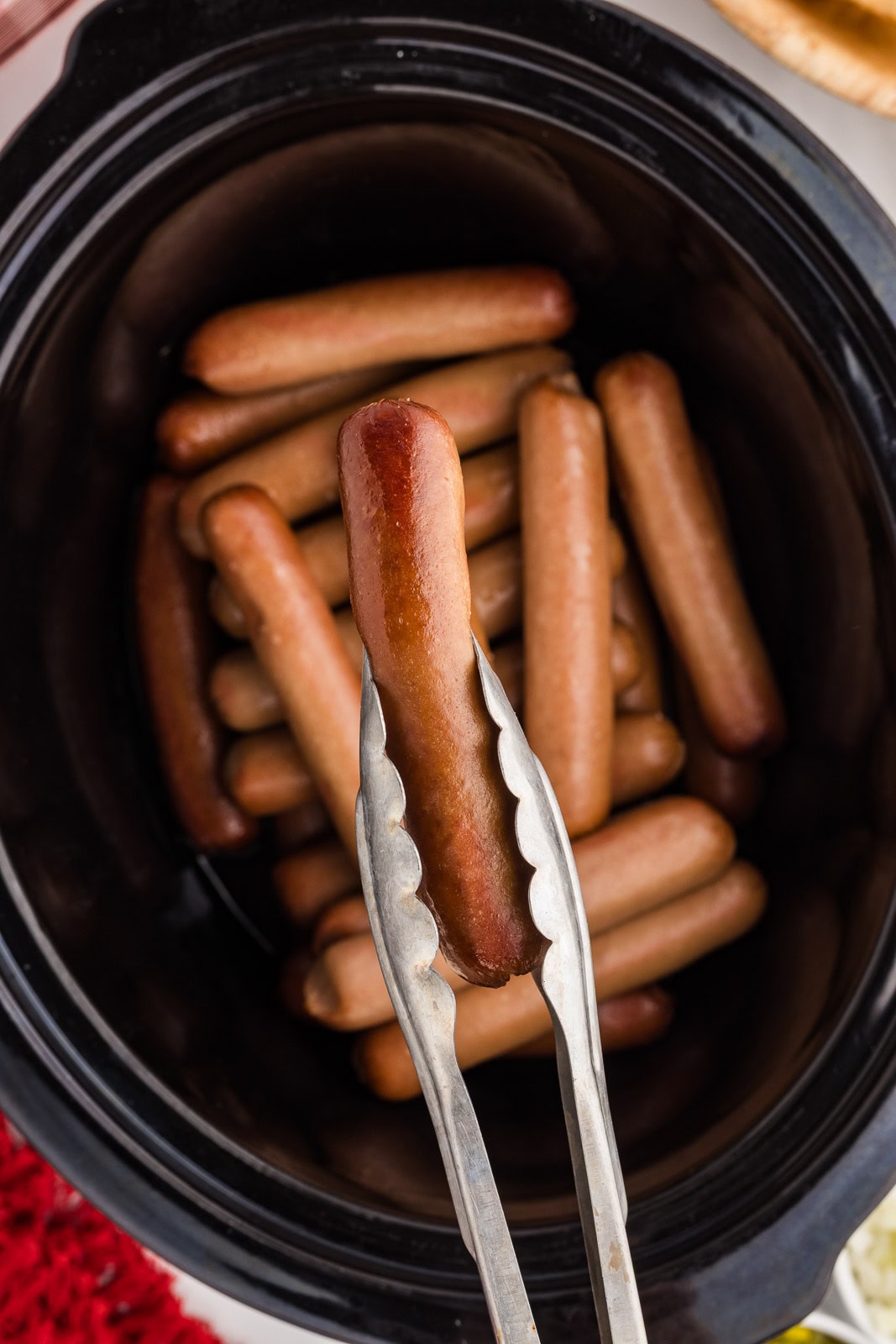 black slow cooker with 23 hot dogs cooked with silver prongs holding 1 hot dog