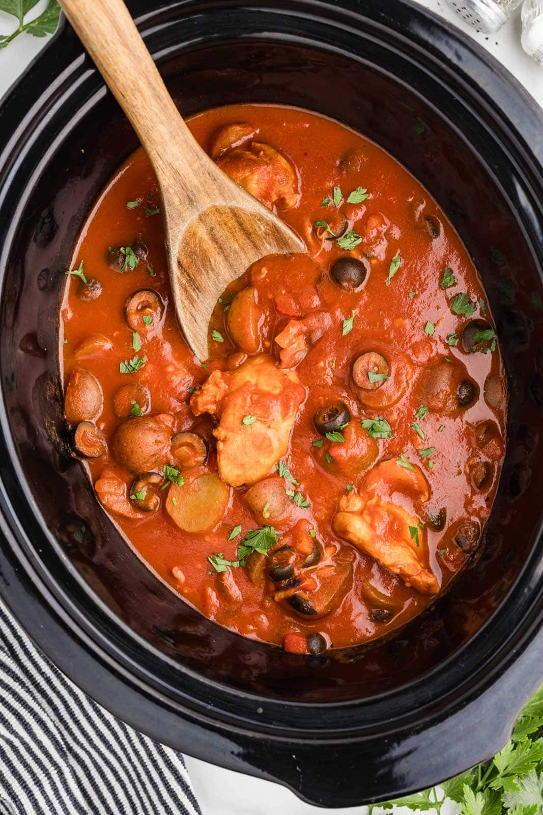 black slow cooker of finished chicken Cacciatore with wooden spoon