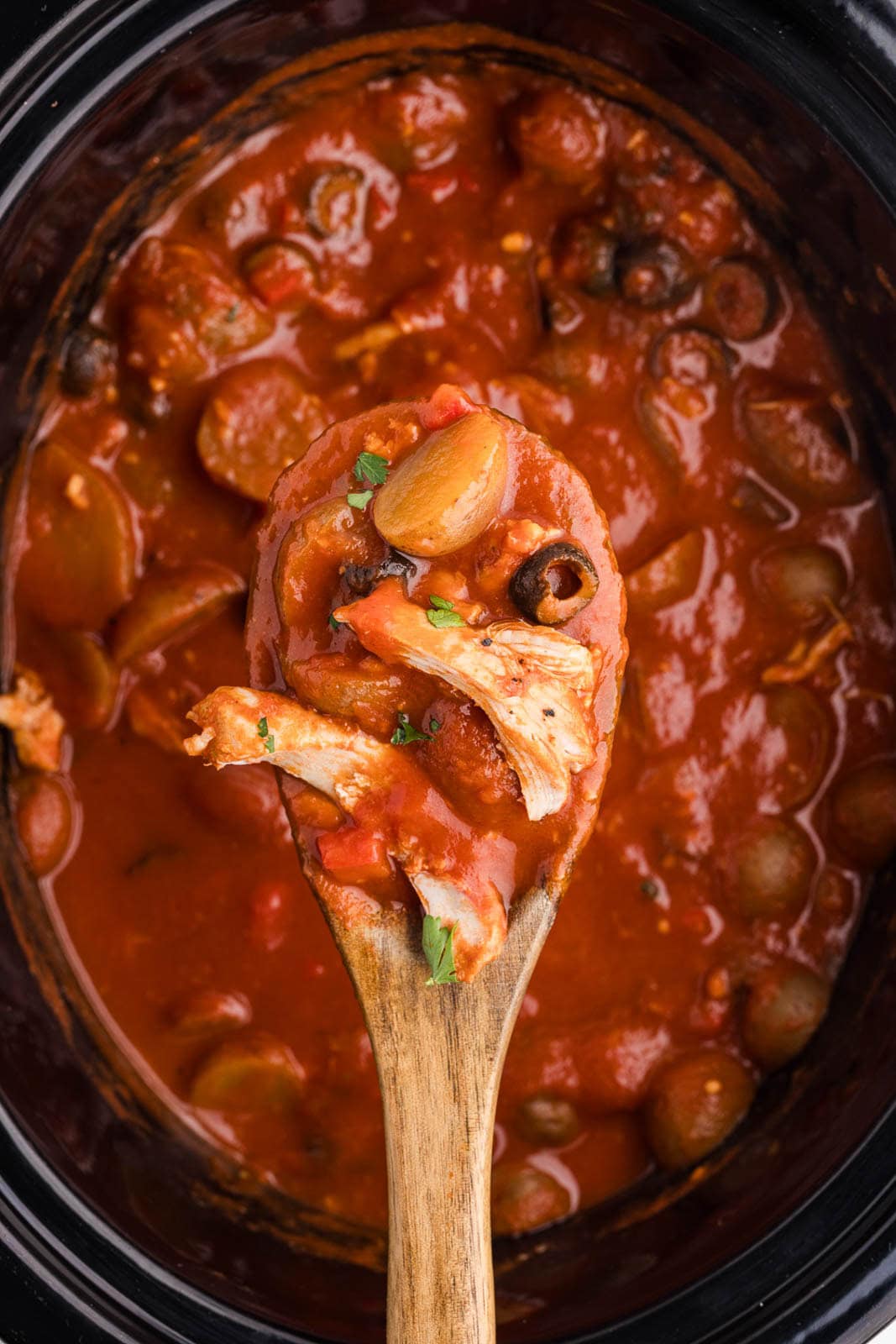 closeup of wooden spoon over black slow cooker containing finished chicken Cacciatore