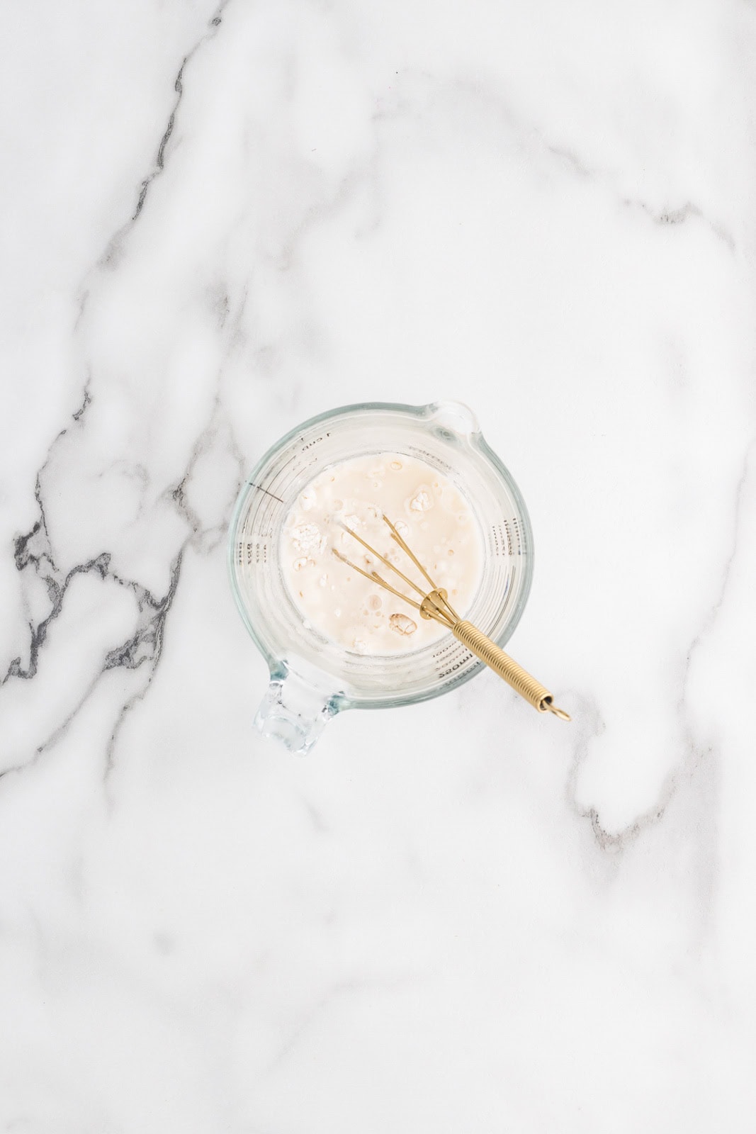 overhead view of glass measuring cups of tapioca flour and water, with gold whisk