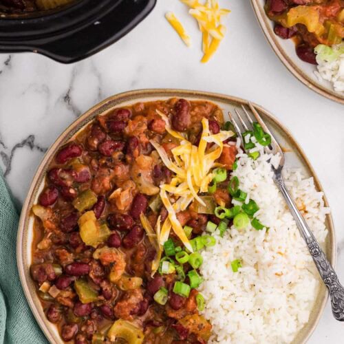 tan rimmed dinner plate of red bean mixture with rice and silver fork, with another plate, green onions, and black slow cooker in background