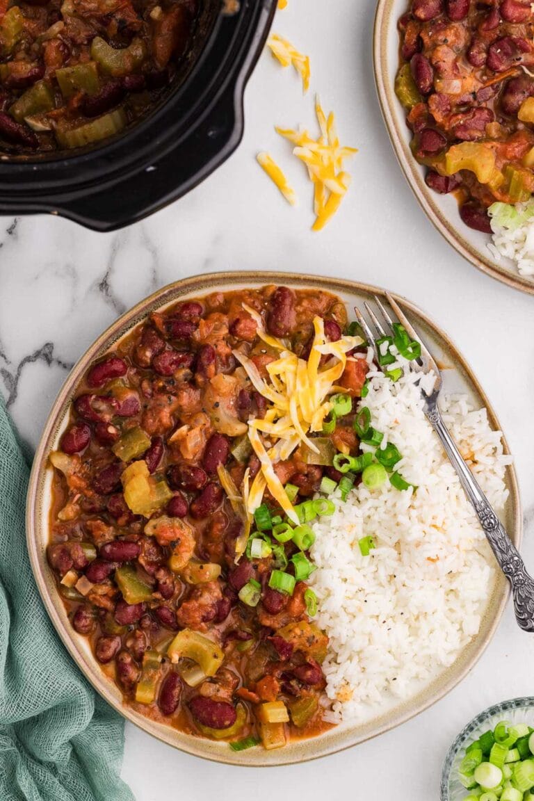 tan rimmed dinner plate of red bean mixture with rice and silver fork, with another plate, green onions, and black slow cooker in background