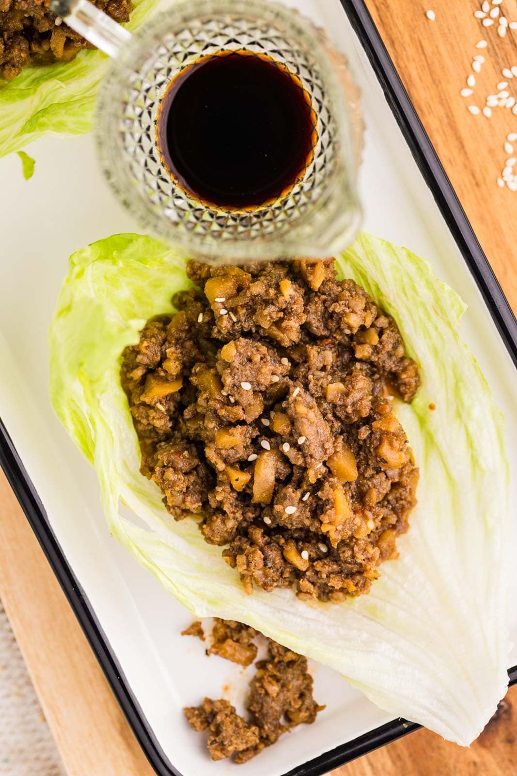 overhead view of white serving platter with one lettuce wrap filled with pork mixture and glass container or soy sauce