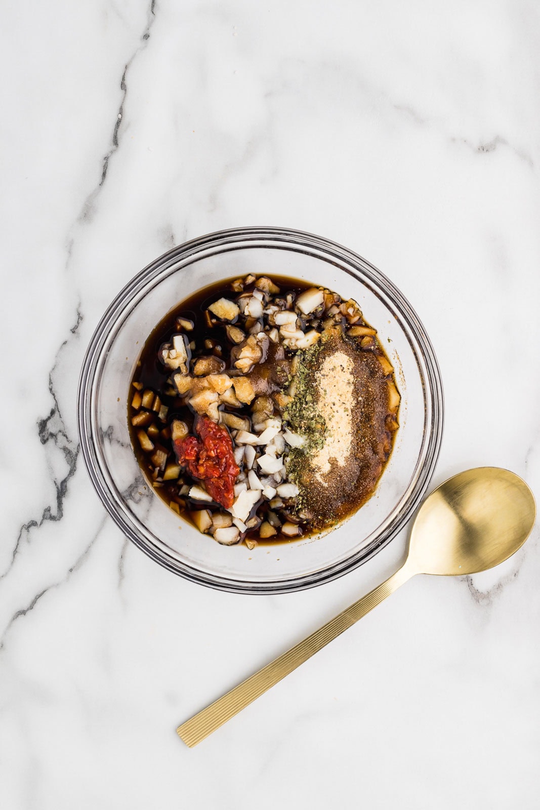 glass bowl with remaining ingredients, minus the lettuce, with gold spoon on side