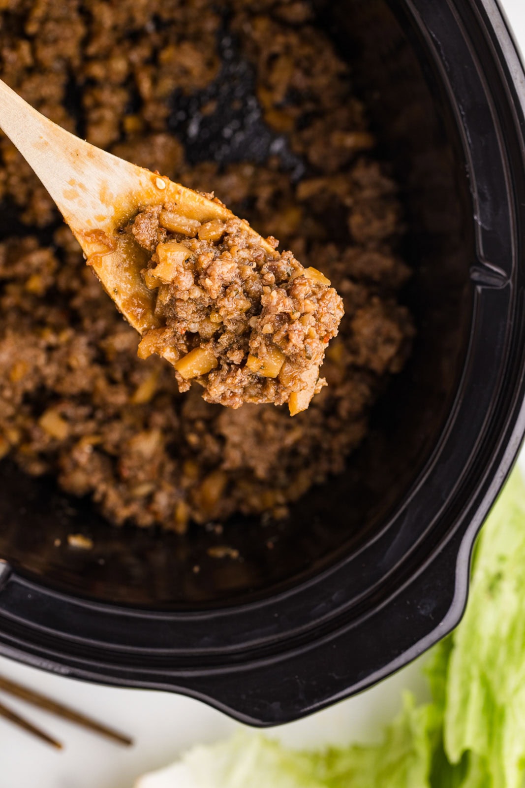 closeup view of wooden spoon with pork mixture with black slow cooker in background