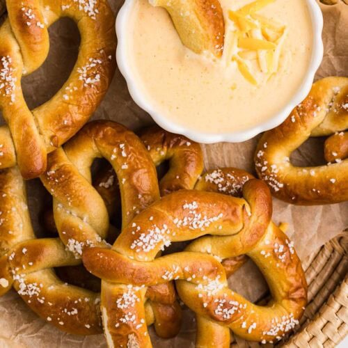overhead new of basket of soft pretzels with small white bowl of cheese dip and portion of pretzel in dip