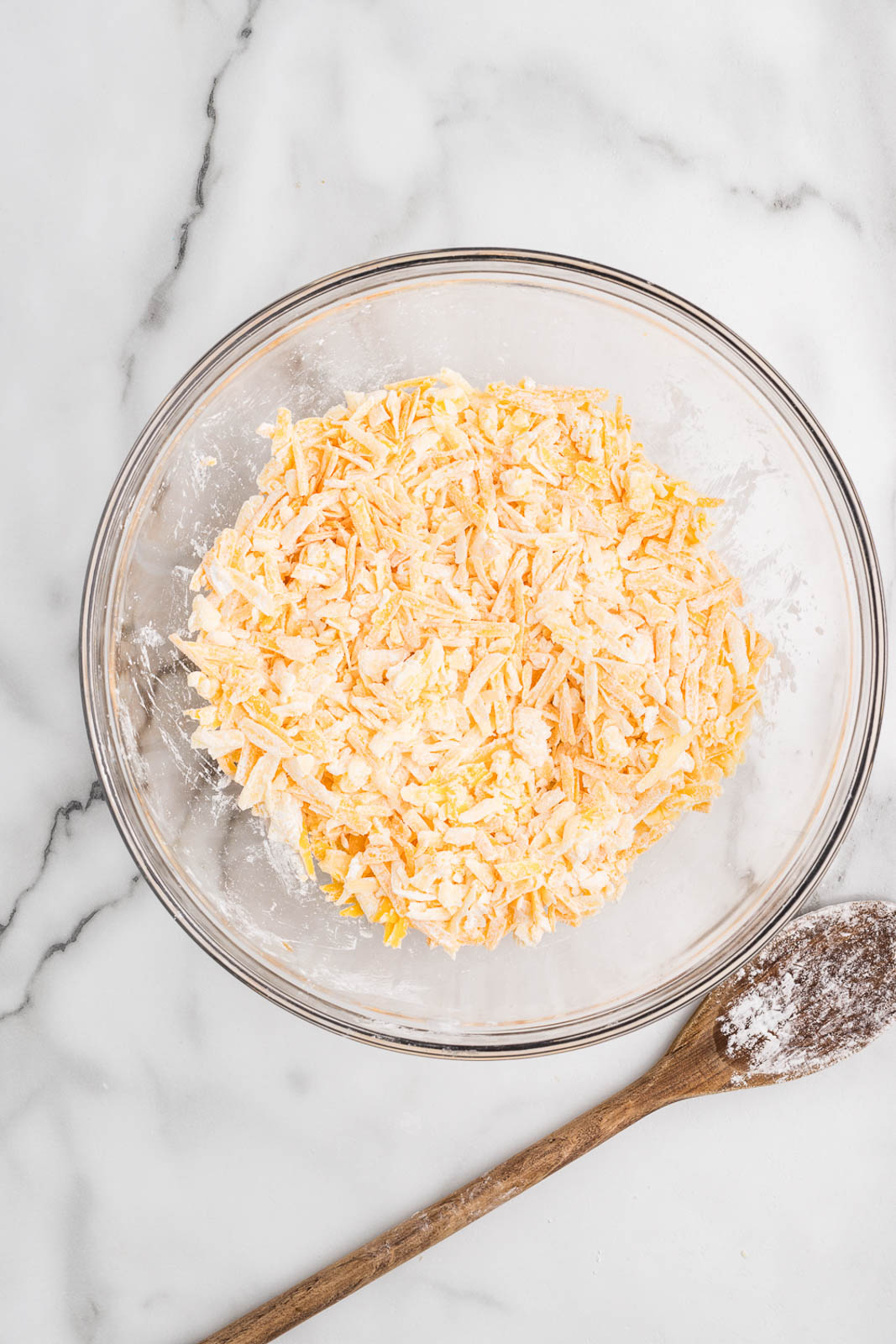 glass bowl of glass bowl of cheese coated with cornstarch with wooden spoon covered with cornstarch on side