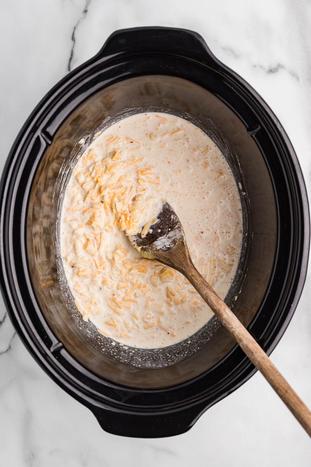 black slow cooker with all ingredients with wooden spoon inserted