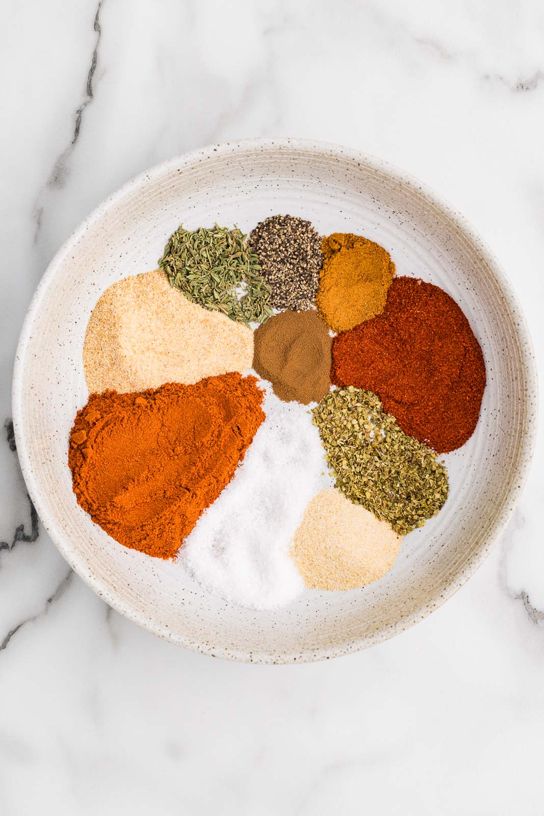 White bowl with seasonings to include paprika, garlic powder, salt, onion powder, thyme, oregano, black pepper, cayenne and instant cofee