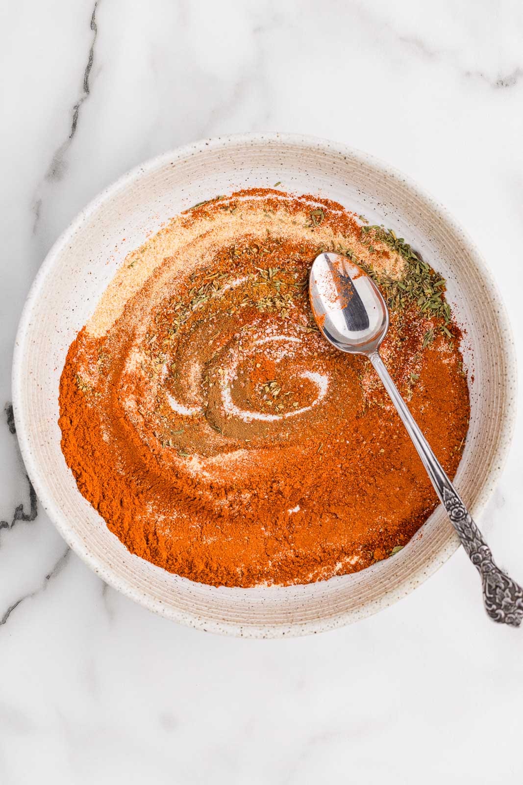 white bowl with seasonings with silver spoon mixing seasonings