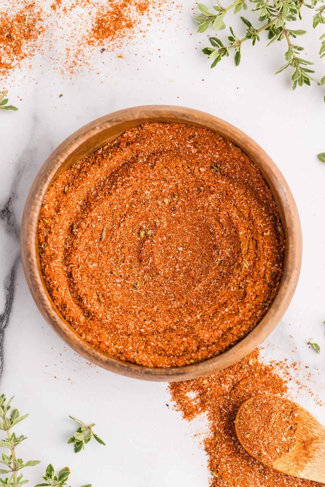wooden bowl with mixed seasonings with wooden spoon and seasoning on side with dried thyme