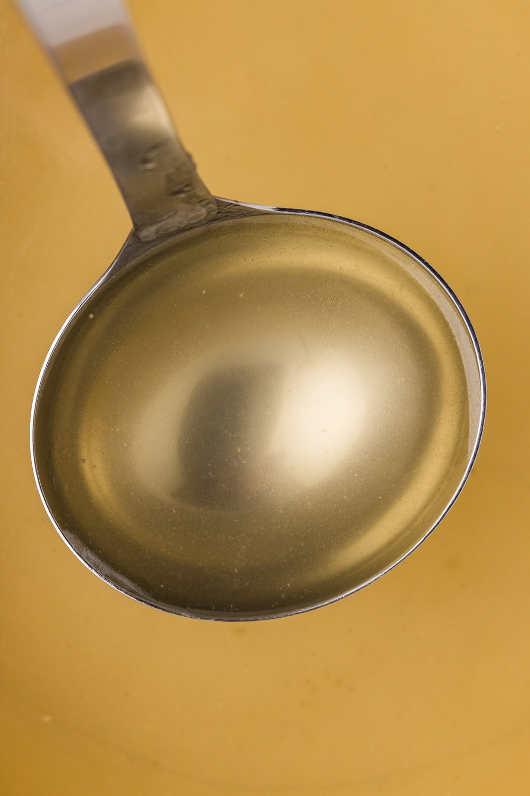 closeup of strained broth in silver ladle over broth in the background