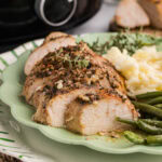 closeup of green dinner plate containing sliced turkey breast, mashed potatoes and green beans, with slow cooker in the background