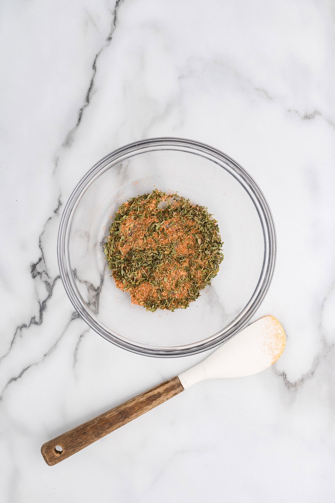 glass bowl with seasonings and wooden handled spatula on side