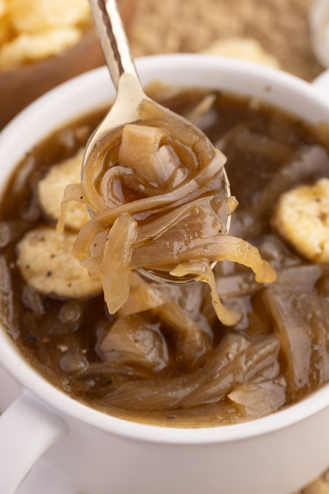 closeup view of white soup cup of onion soup and silver spoon containing soup in forefront