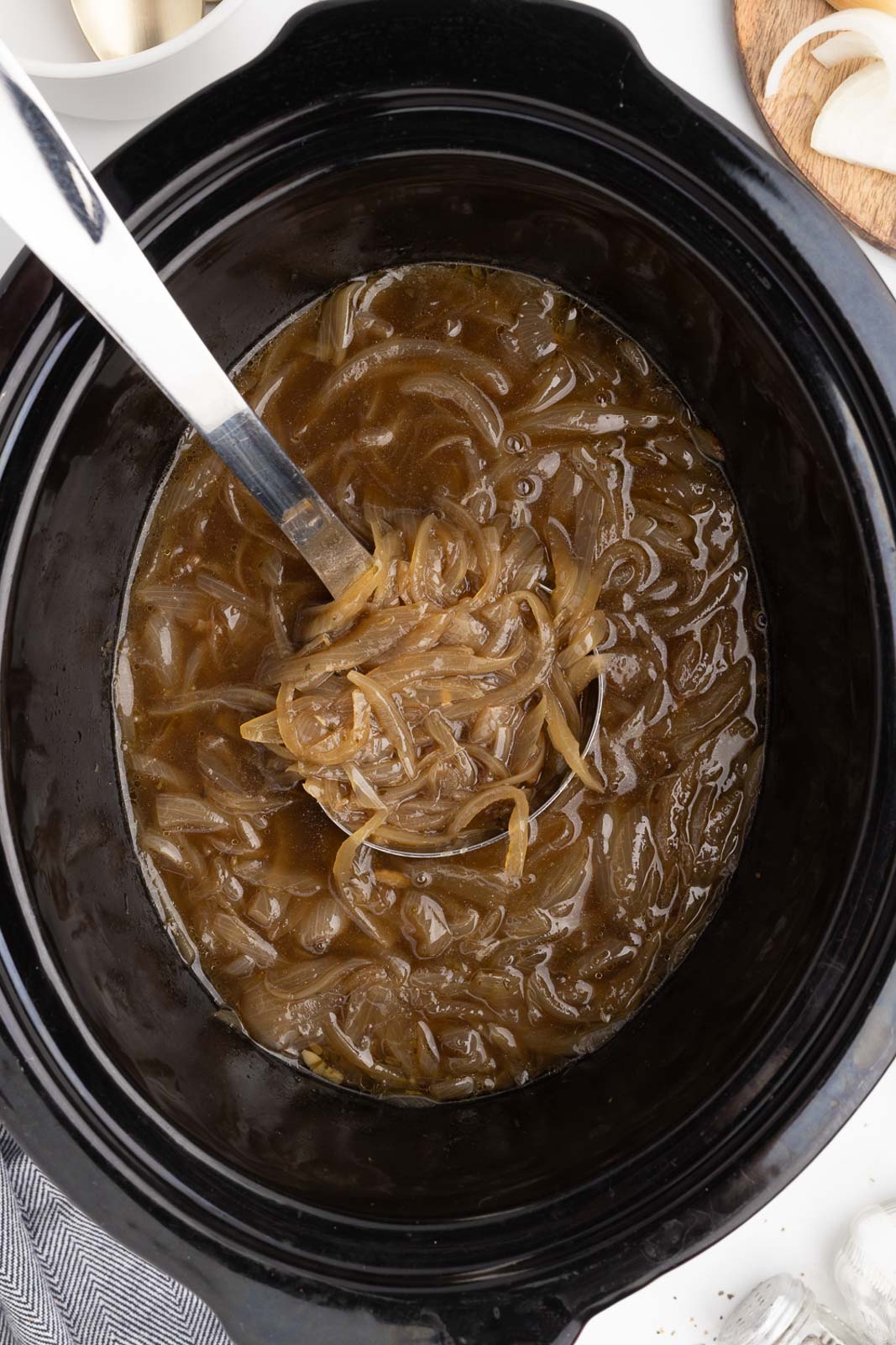 black slow cooker of cooked onion soup with large silver ladle inserted