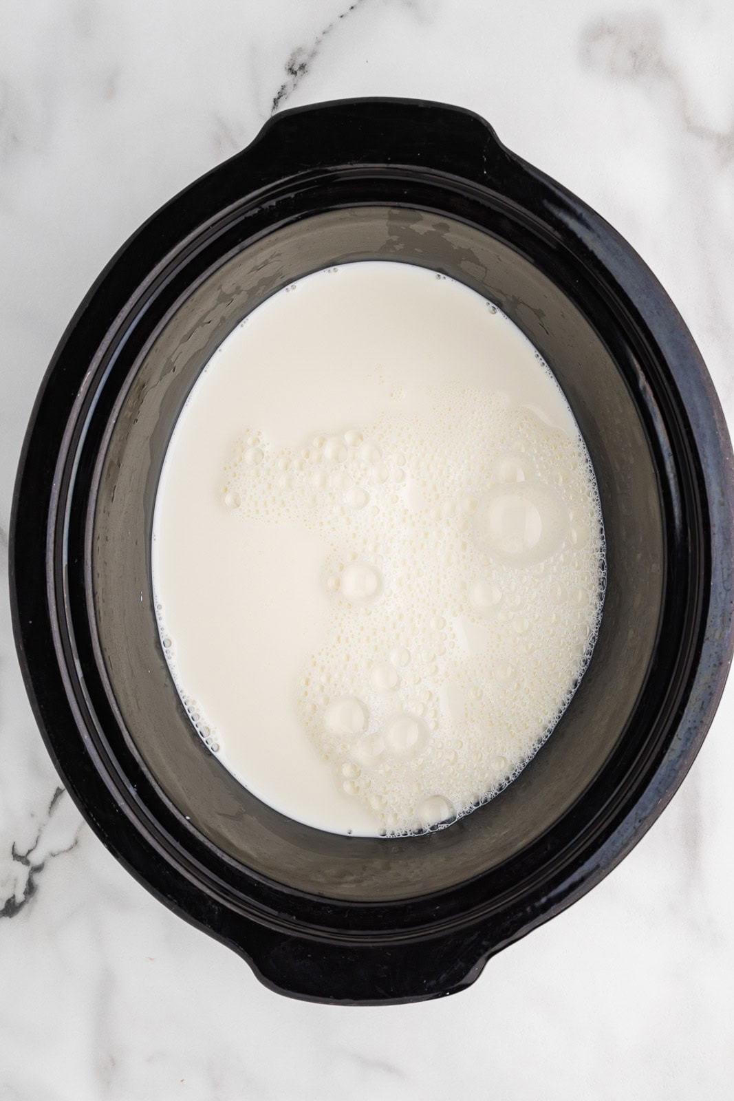 overhead view of black slow cooker containing milk and heavy cream
