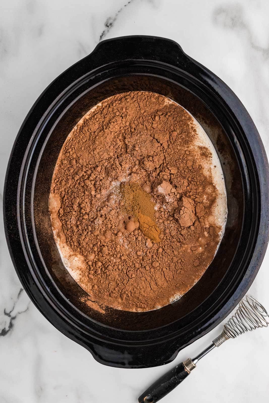 overhead view of black slow cooker containing milk and heavy cream and all other dry ingredients except for chocolate chips