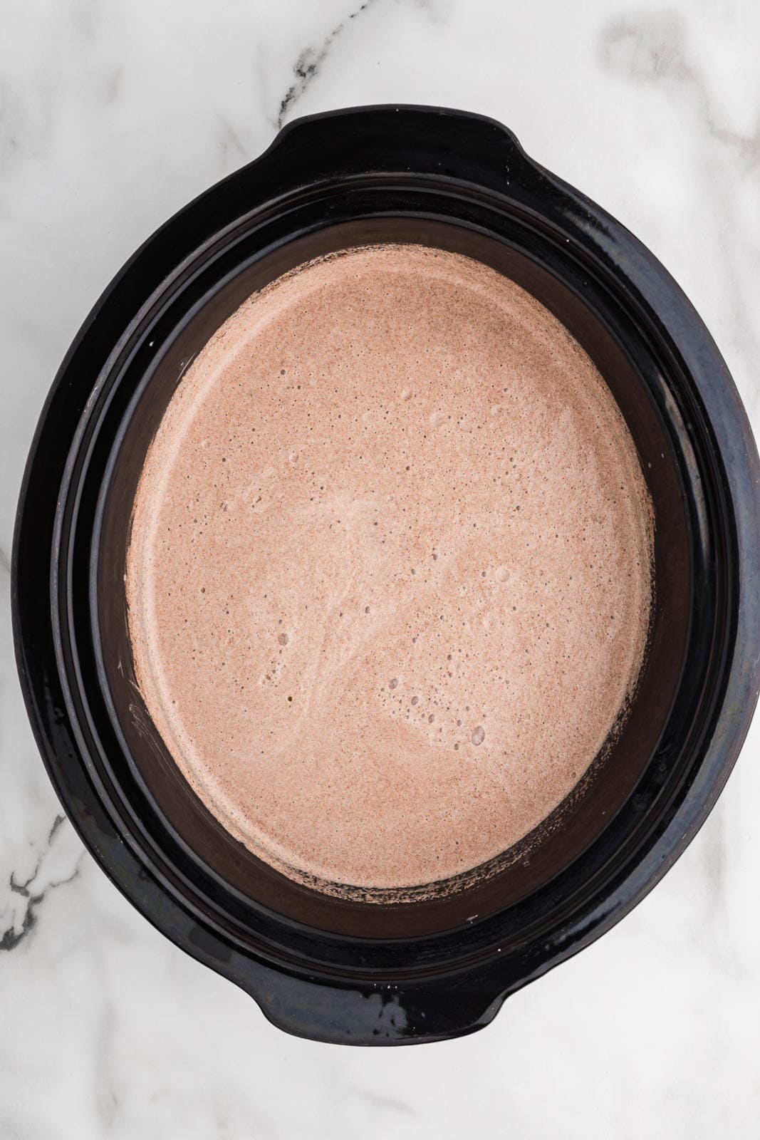 overhead view of black slow cooker containing all ingredients, except chocolate chips, after mixing