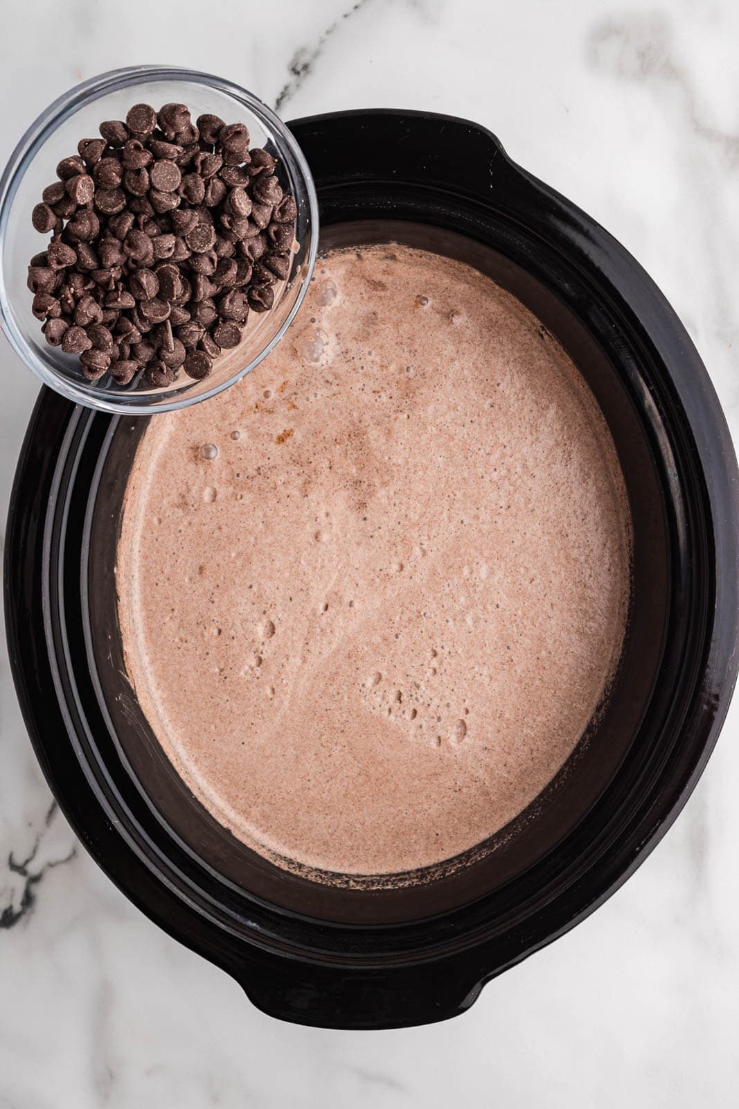overhead view of black slow cooker with mixed ingredients with bowl of chocolate chips
