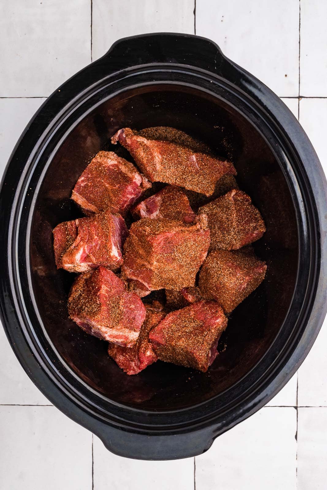 black slow cooker filled with chuck roast chunks sprinkled with spice blend